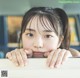 A young girl peeking over a counter with her hand on her chin.