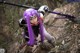 A woman with purple hair holding a sword in the woods.