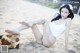 A woman in a white bathing suit sitting on a beach.