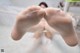 A woman in a white dress is holding her bare feet up.